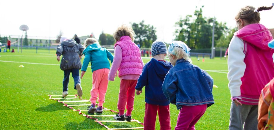 Kinder Springen über eine auf dem Boden liegende Leiter