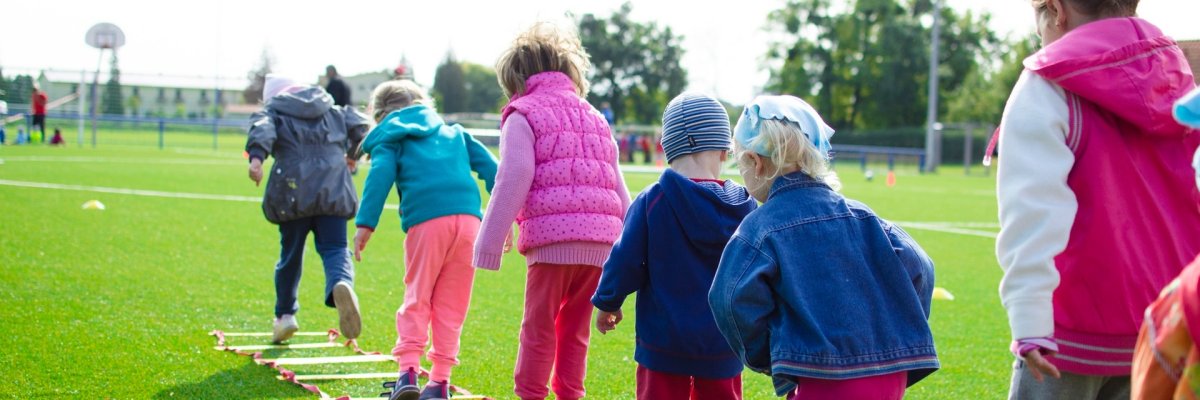 Mehrere Kinder springen über eine auf dem Boden liegende Leiter Mehrere Kinder springen über eine auf dem Boden liegende Leiter